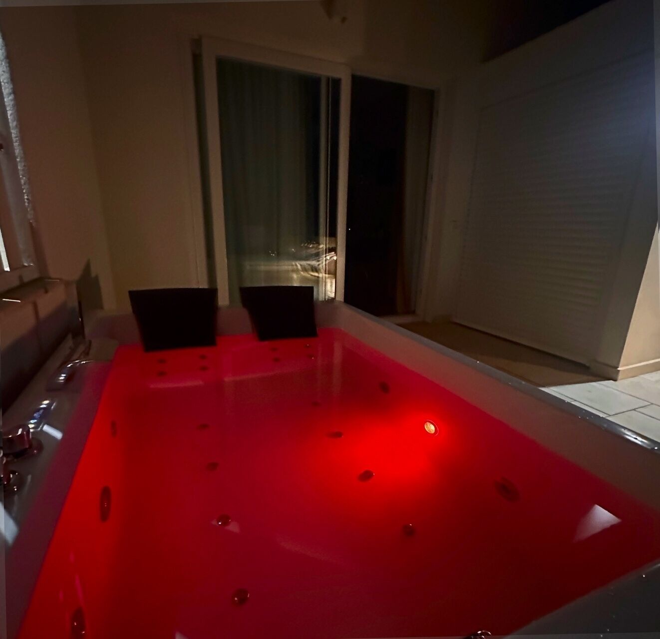A red hot tub with two chairs, a window, and a closed sliding door.