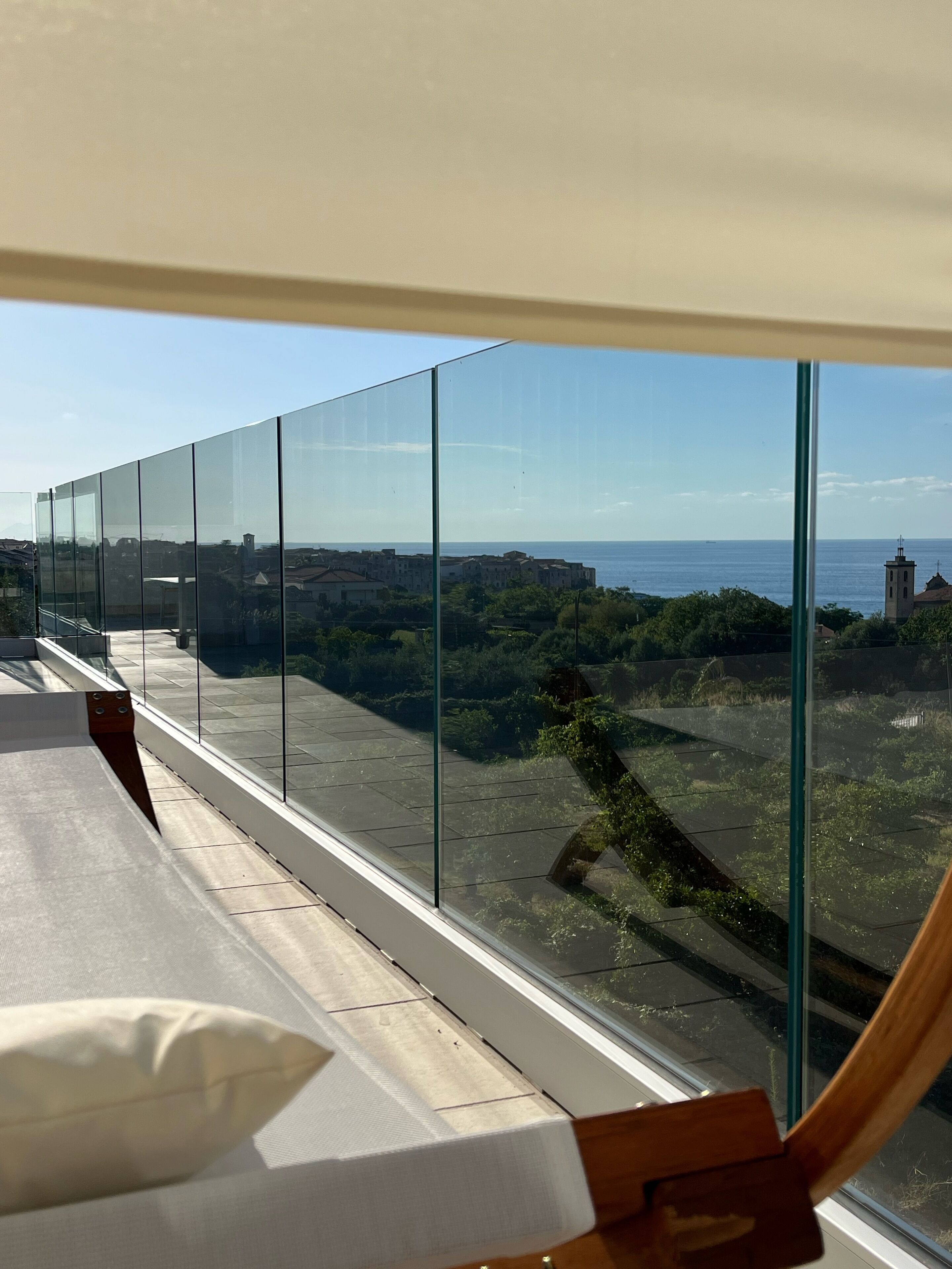 A balcony with a glass railing overlooking a coastal town and the sea.