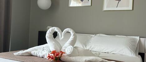 A neatly made bed with white linens and a brown patterned throw. Two towels are arranged in the shape of swans on the bed.