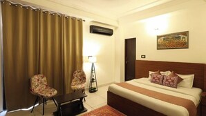 A hotel room with a large bed, two floral armchairs, a small table, a floor lamp, and a painting on the wall. - Hotel Amarah (Jaipur)
