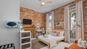 A modern room with a brick wall, a bed, a desk, a TV, and a balcony with a view. - 1 bedroom, 1 bathroom studio apartment in Downtown Augusta. The sleeping arrangements for this unit is a full sized bed. (Augusta)