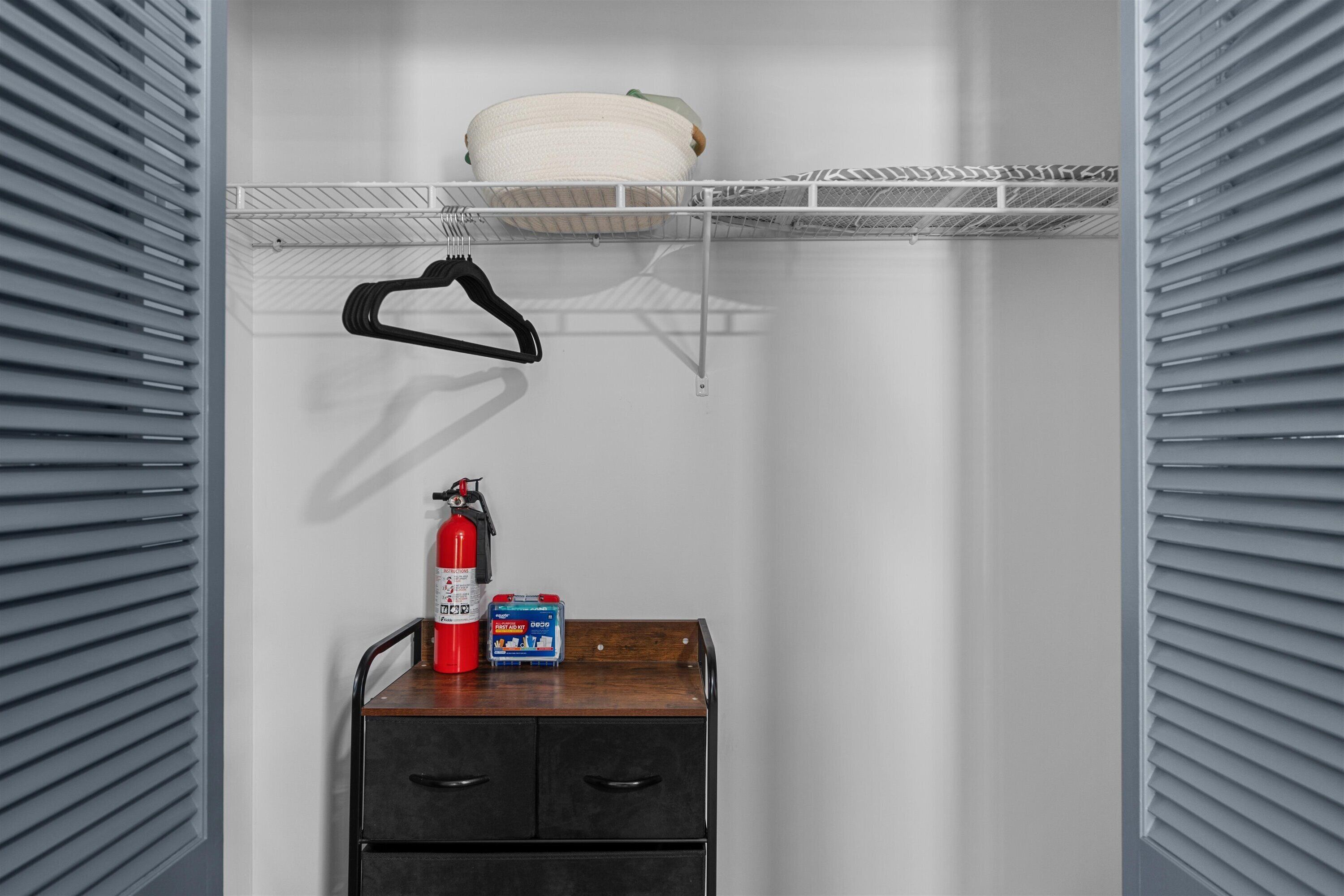 A storage closet with a fire extinguisher, a first aid kit, and a basket on a shelf.