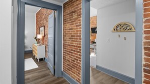 A hallway with a brick wall, a white door, and a white wall with a decorative metal piece. - 1 bedroom, 1 bathroom suite in Downtown Augusta. The sleeping arrangements for this unit are a full size bed and a pull-out couch in the living room. (Augusta)