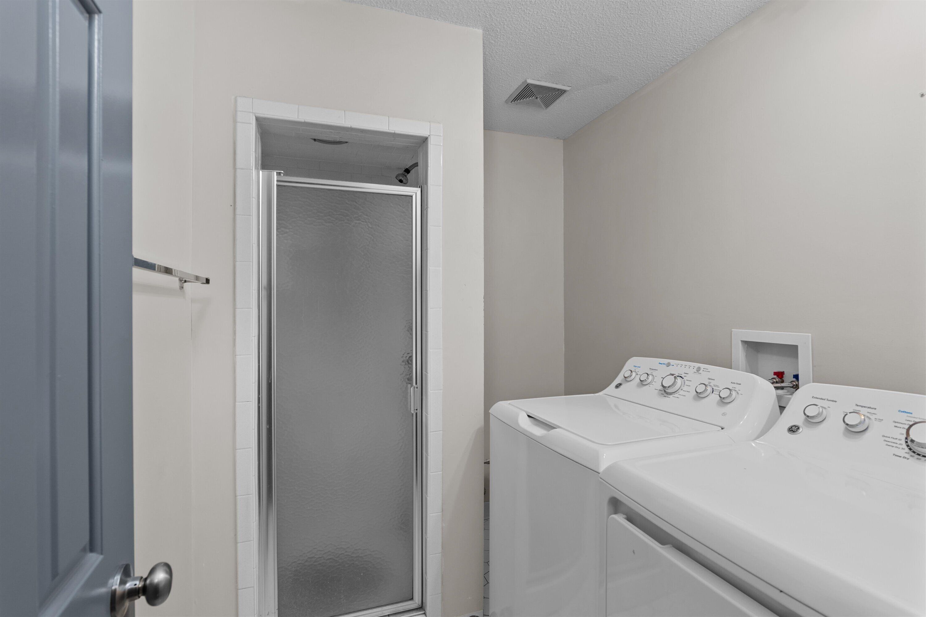 A laundry room with a door leading to a shower, and two front-loading washing machines.