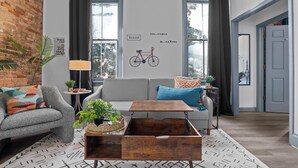 A modern living room with a grey sofa, a wooden coffee table, and a wall with motivational quotes and a bicycle illustration. - 1 bedroom, 1 bathroom suite in Downtown Augusta. The sleeping arrangements for this unit are a full bed and a pull-out couch in the living room. (Augusta)