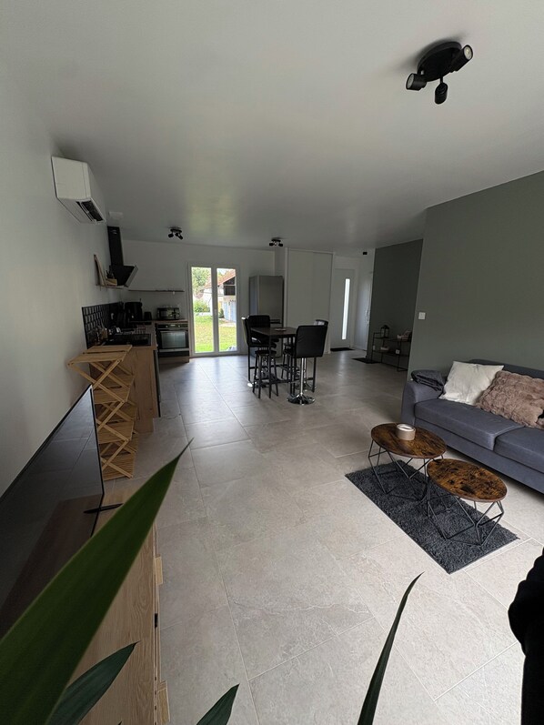 Ein modernes Wohnzimmer mit grauem Sofa, Couchtisch und Essbereich mit Tisch und Stühlen. Es gibt eine Küchenzeile mit Herd und Mikrowelle.