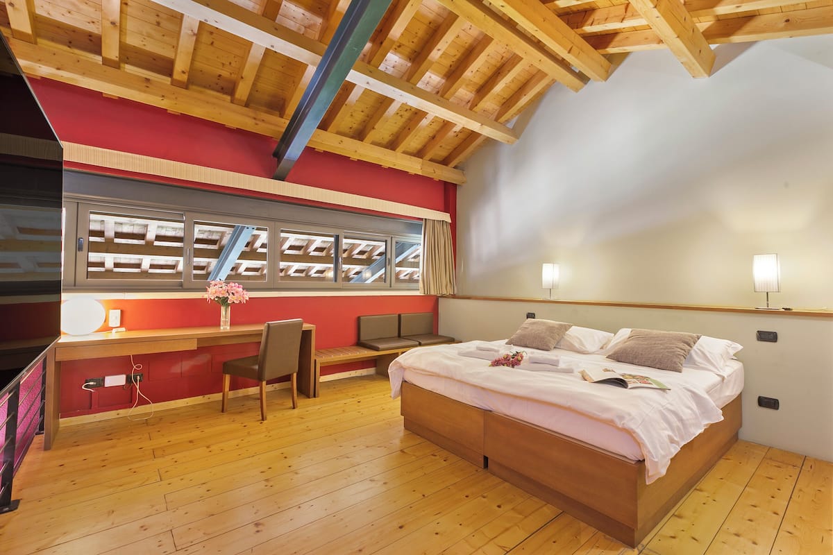 Un dormitorio con techo de madera, una cama con almohadas, un escritorio con silla y una ventana con persianas.