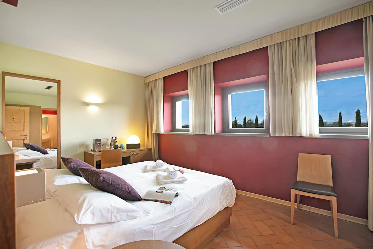 Una habitación de hotel con una cama, una silla, un escritorio con lámpara y una ventana con cortinas.