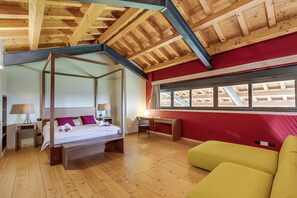 Cozy retreat with a four-poster bed, desk, and sofa, set against a sloped ceiling with exposed beams and large windows.