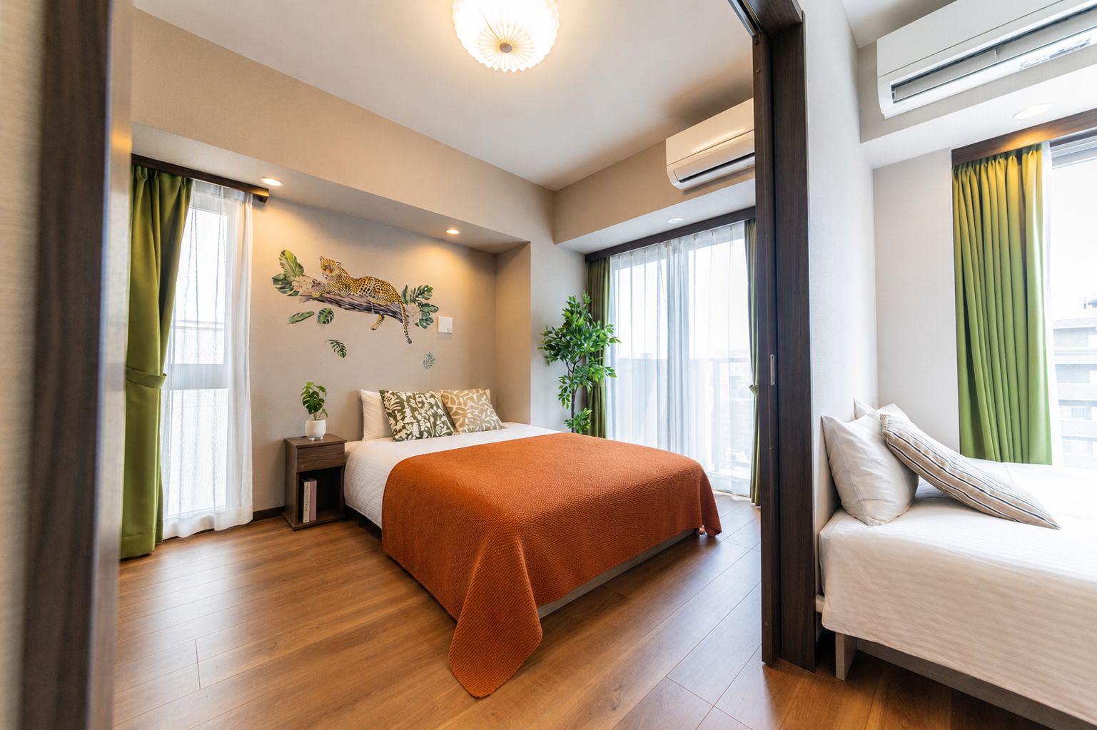 A hotel room with a bed, a sofa, a wall mural, and an air conditioning unit.
