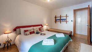 A neatly arranged bedroom with a large bed, bedside lamps, a wooden bench, and a door. - Montagne E Coccole (Pre-Saint-Didier)