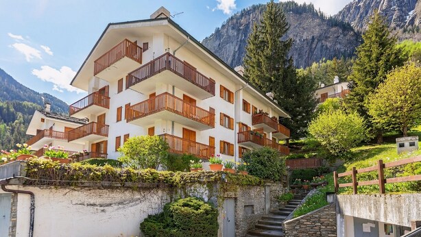 A multi-story hotel with balconies, a stone staircase, and a mountainous backdrop. - Montagne E Coccole (Pre-Saint-Didier)