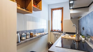 A compact kitchen with white tiles, a black countertop, and wooden shelves. - Montagne E Coccole (Pre-Saint-Didier)