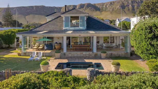 A two-story house with a covered patio, a swimming pool, and a view of mountains. - 4-bedroom house overlooking the sea on the cliff path in Hermanus (Hermanus)