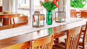 A dining area with a wooden table, chairs, hanging pendant lights, and a vase with flowers. - 4-bedroom house overlooking the sea on the cliff path in Hermanus (Hermanus)