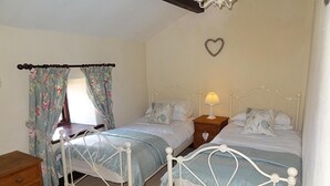 A bedroom with two single beds, a wooden dresser, a nightstand with a lamp, and a heart-shaped decoration on the wall.