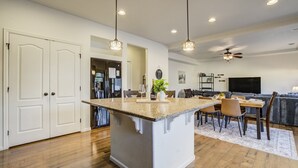 Une cuisine spacieuse dotée d’un îlot central, de planchers en bois, de luminaires suspendus et d’un coin repas avec des chaises et une table.