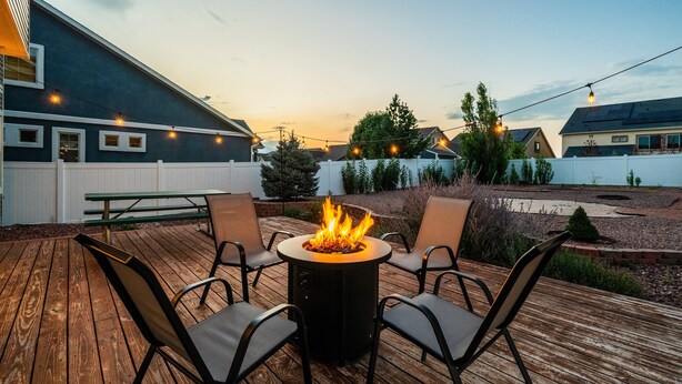 Une terrasse dotée d’un foyer central de forme ronde, entouré de chaises, et offrant une vue sur un jardin aménagé et un quartier résidentiel.