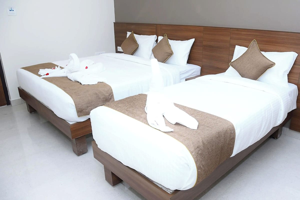Deux lits simples avec des têtes de lit en bois, du linge de lit blanc et des coussins décoratifs marron.