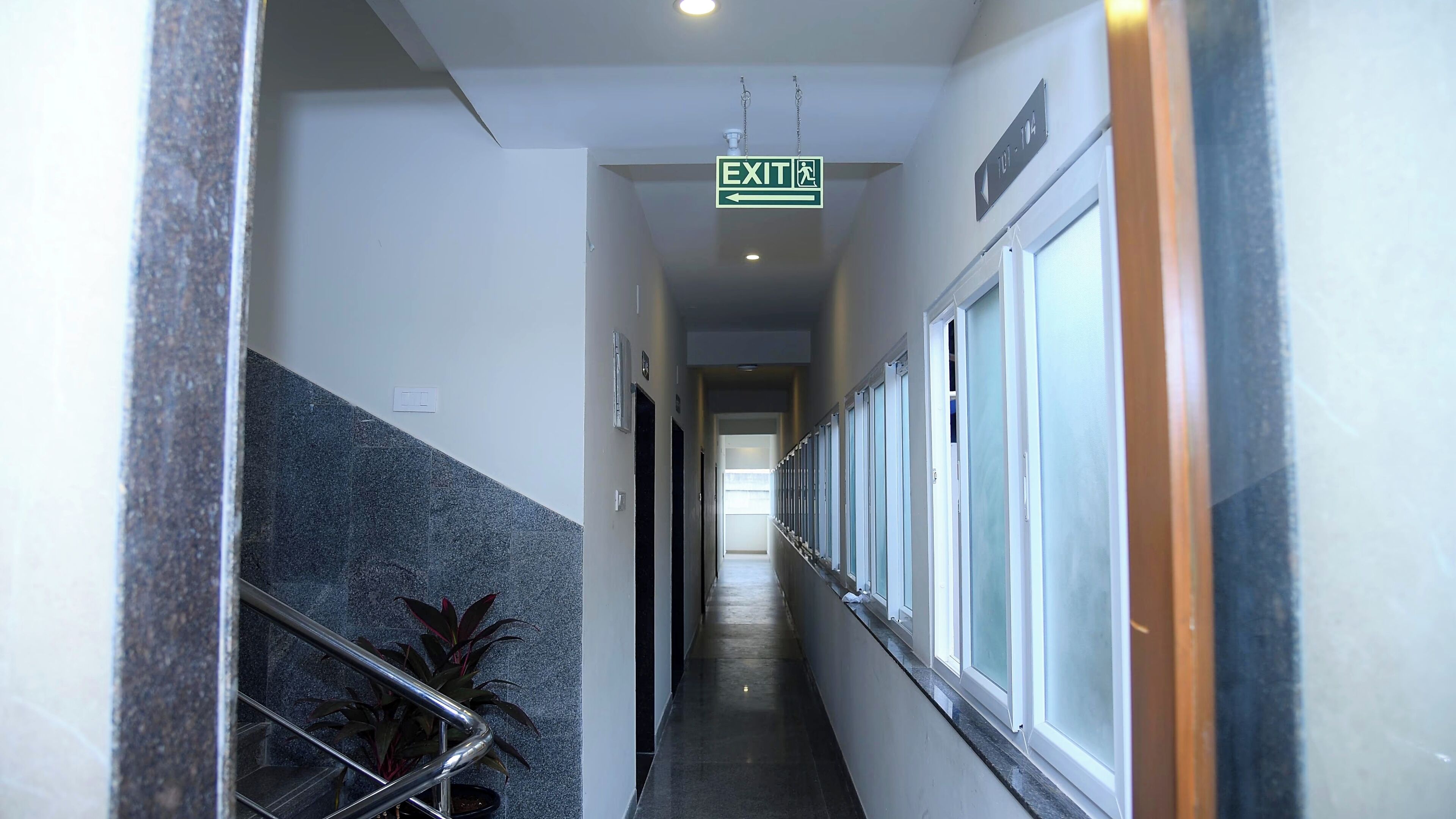 A hallway with an exit sign, a staircase, and a plant.