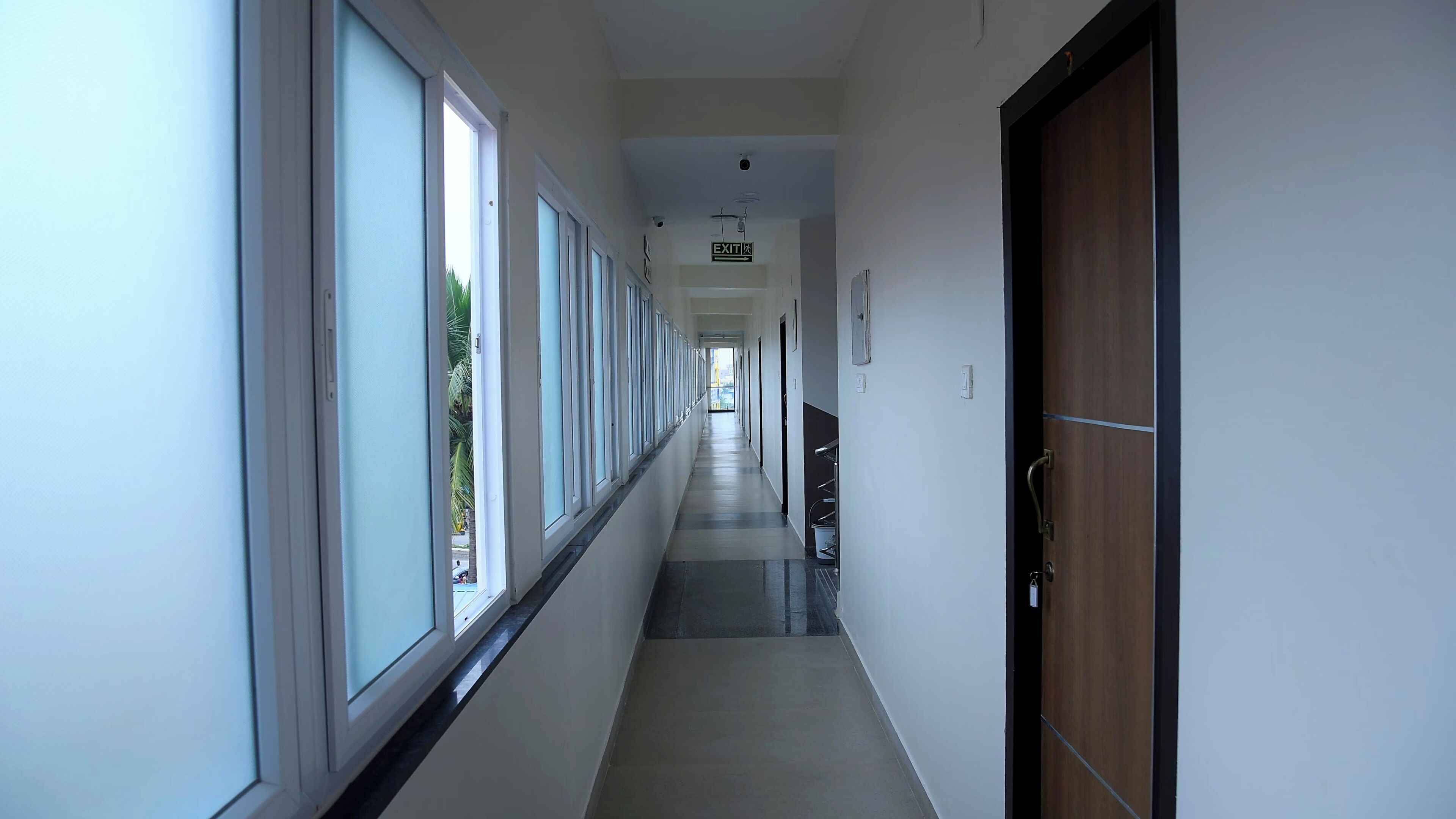 A long, narrow hallway with large windows on one side and a door at the end.