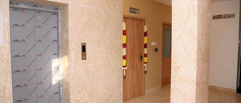 A hallway with a lift door, a wooden door labeled "MANAGER", and a wall with a bulletin board.