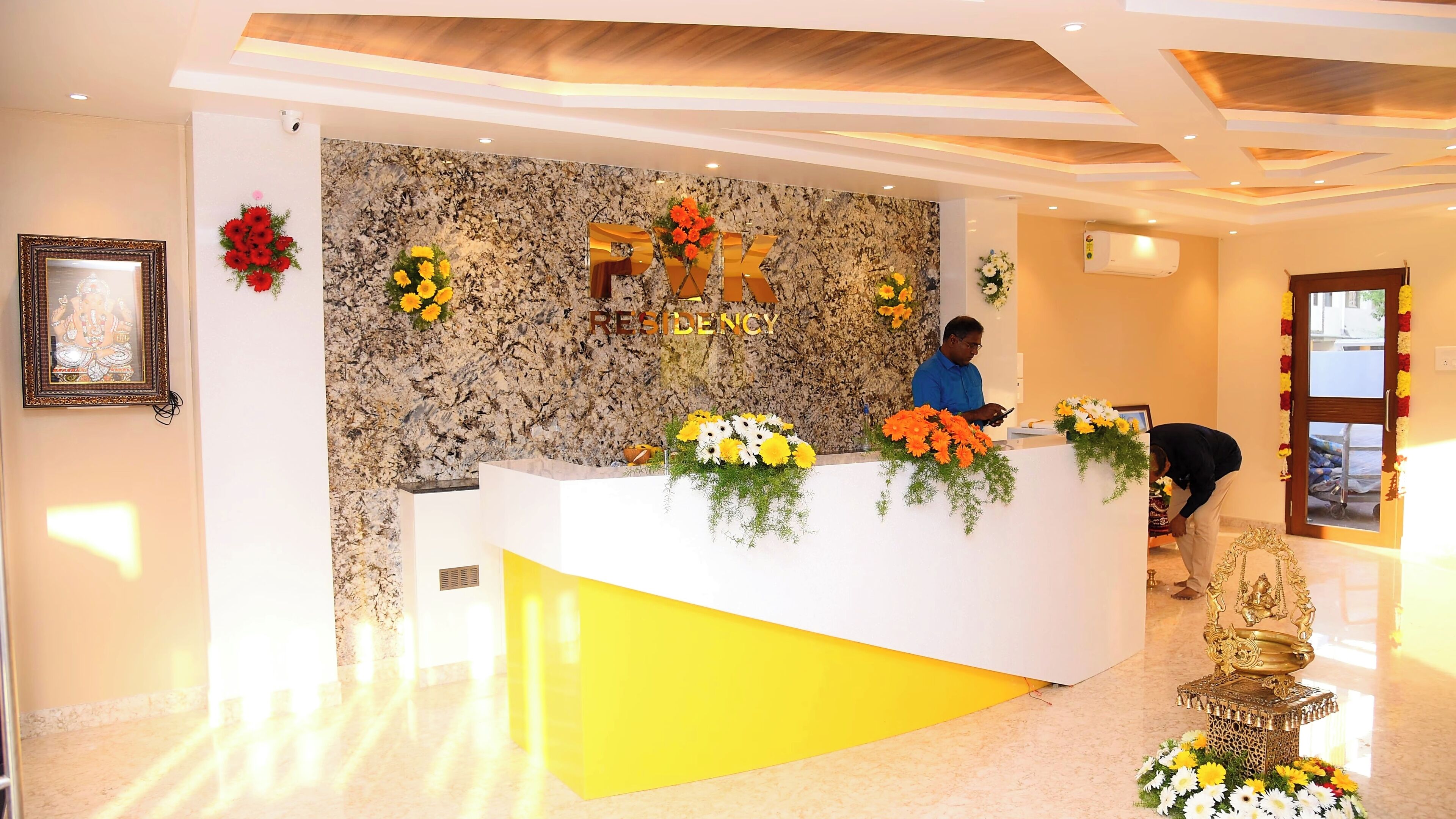 A reception desk with a marble wall backdrop, a framed picture on the left, and a golden statue in the foreground.