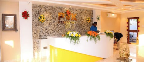 A reception desk with a marble wall backdrop, a framed picture on the left, and a golden statue in the foreground.