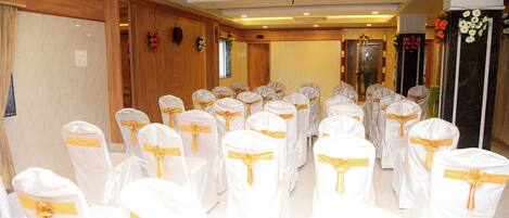 Un salón de conferencias con filas de sillas blancas con cintas doradas, paneles de madera y decoraciones florales.
