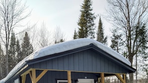 A cabin with a wooden deck and a covered porch, surrounded by snow and trees.