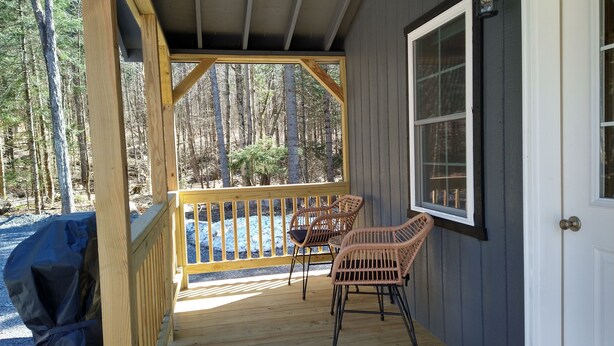 A covered porch with two wicker chairs, a grill, and a view of a forest.