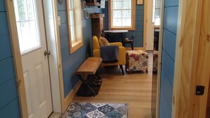 A cozy interior with a wooden bench, a small table, and a patterned rug leading to a room with a blue wall and wooden ceiling beams.