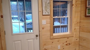A wooden cabin interior with a white door, a window with a wooden railing, and a welcome sign.