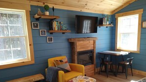 A cozy room with a fireplace, a yellow armchair, a small table, and a television mounted on the wall.