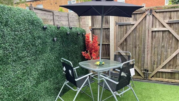 A patio with a round glass table, four chairs, and a black umbrella. - 2br-sleeps3 -family Friendly -free Parking -garden (Nottingham)
