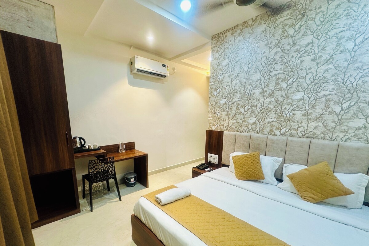 A hotel room with a bed, a desk, a chair, an air conditioner, and a nightstand.