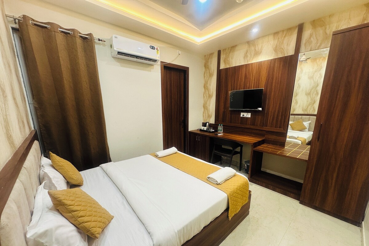 A hotel room with a bed, a desk, a TV, and an air conditioning unit.