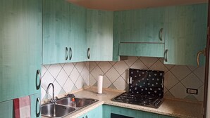 A kitchen with teal cabinets, a gas stove, a sink, and a tiled backsplash. - La Casa di Amalia in Ponte (Budoni)