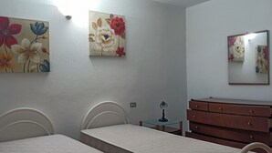 A bedroom with two single beds, a wooden dresser, a small table with a lamp, and floral artwork on the walls. - La Casa di Amalia in Ponte (Budoni)