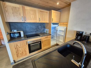 A modern kitchen with wooden cabinets, a built-in oven, a microwave, a refrigerator, and a sink with a faucet. - Bright 3-room apartment, close to slopes, pets allowed (Les Deux Alpes)