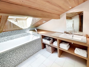 A modern bathroom with a freestanding bathtub, a large mirror, and wooden shelves with towels.