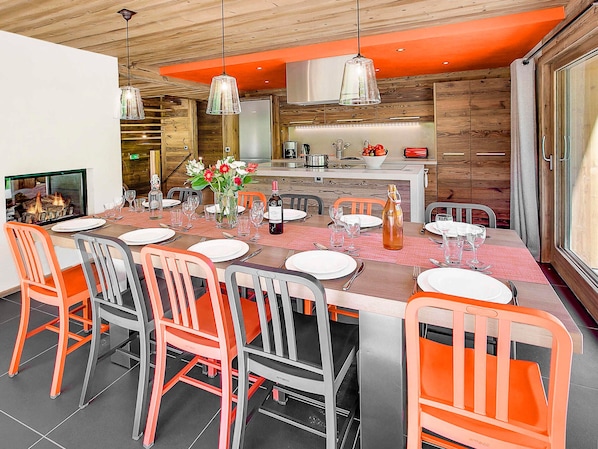 A modern dining area with a wooden table set for six, surrounded by orange and gray chairs.