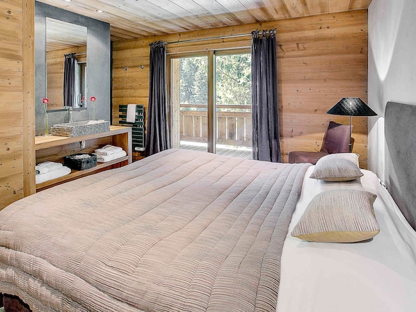 Une chambre dans une cabane en bois, avec un grand lit, une commode, un miroir et un balcon agrémenté de rideaux.