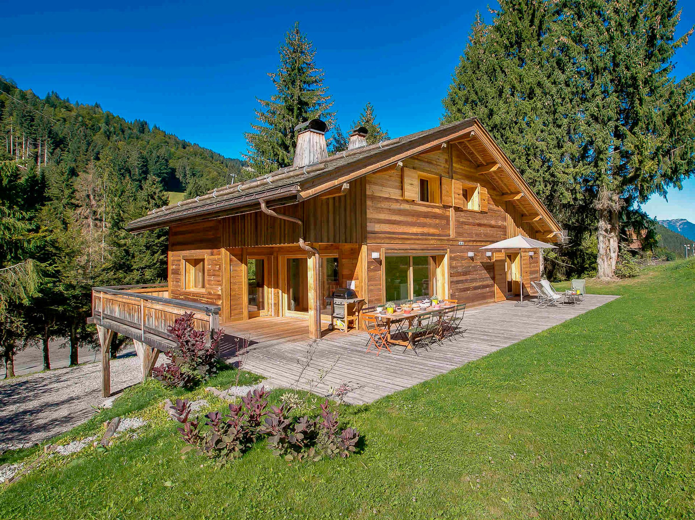 Eine Holzhütte mit einer Terrasse, Sitzgelegenheiten im Freien und einem Blick auf die Berge.