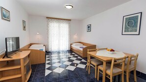 A compact room with a bed, a TV, a dining table with chairs, and a checkered floor. - Apartman Villa Ljiljana 5 (Jadranovo)