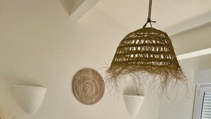 Un dormitori amb un llit gran, roba de llit blanca, una làmpada penjant de fibra natural i un element decoratiu circular fixat a la paret.