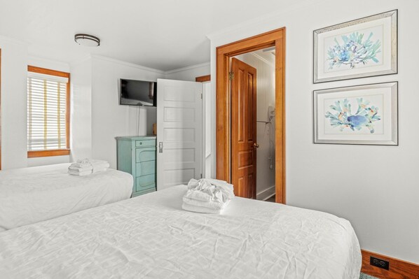 A bedroom with two beds, a television, a wooden door, and two framed floral artworks.