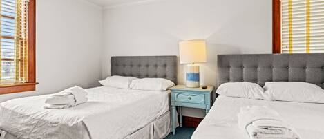 A hotel room with two beds, a nightstand with a lamp, and a window with blinds.