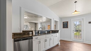 Een moderne keuken met witte kastjes, een granieten aanrechtblad en een vaatwasser. Er is een groot raam met uitzicht op het buiten.