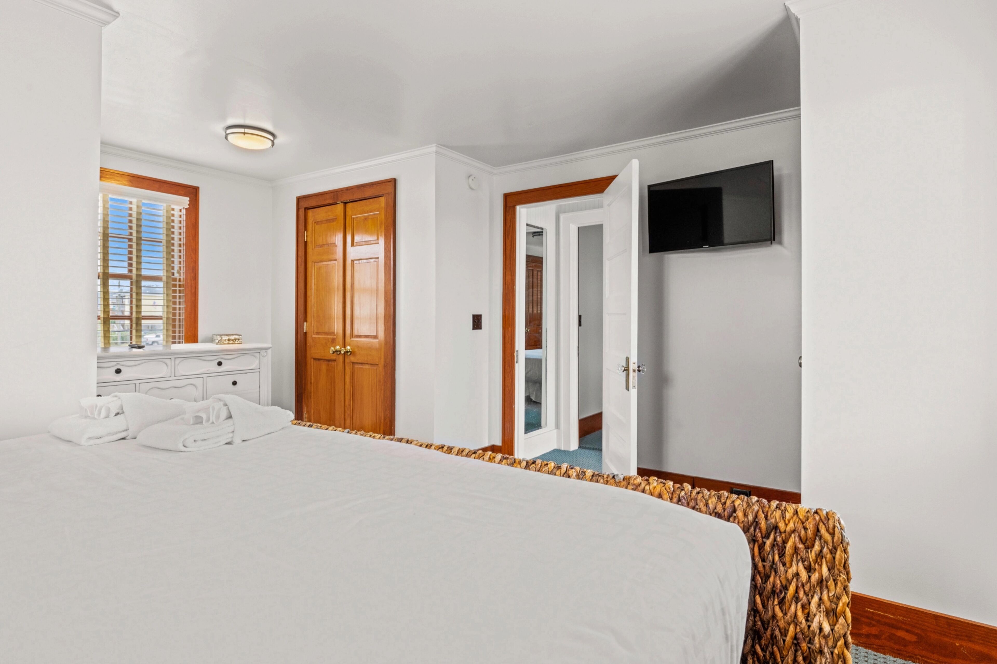 A hotel room with a large bed, a wooden door, a television, and a window with blinds.